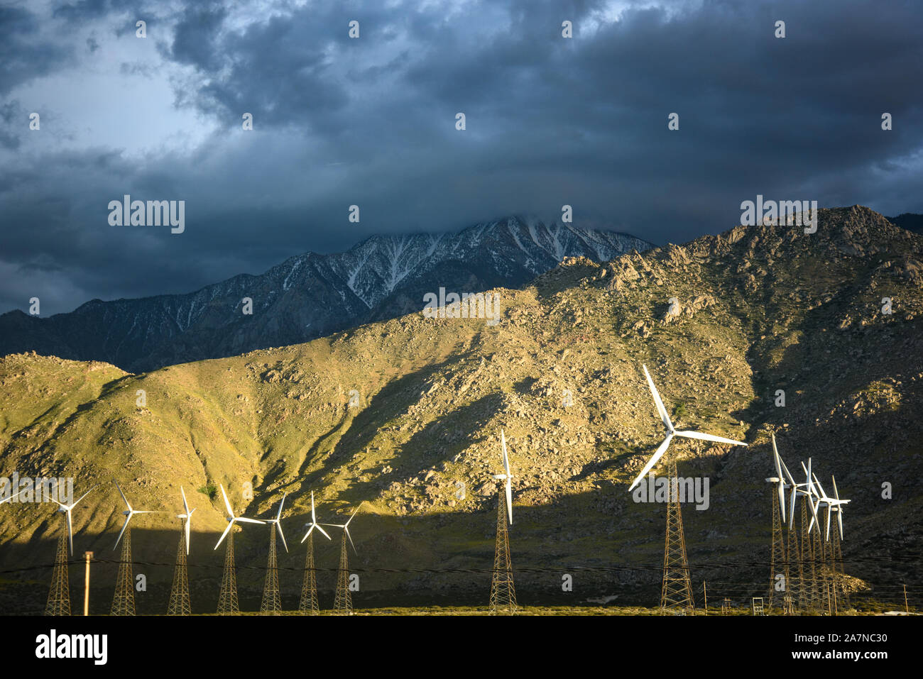 Mulini a vento sono illuminati di fronte al picco di neve montagne in Yucca Valley Foto Stock