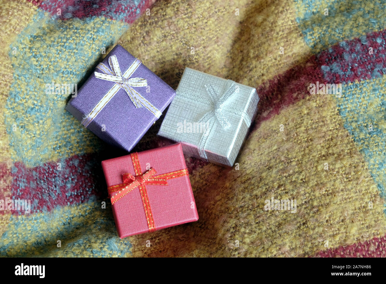 Tre regali di natale in piccole caselle colorate, coperto con nastro con archi, contro uno sfondo di tessuto di lana top view close-up Foto Stock