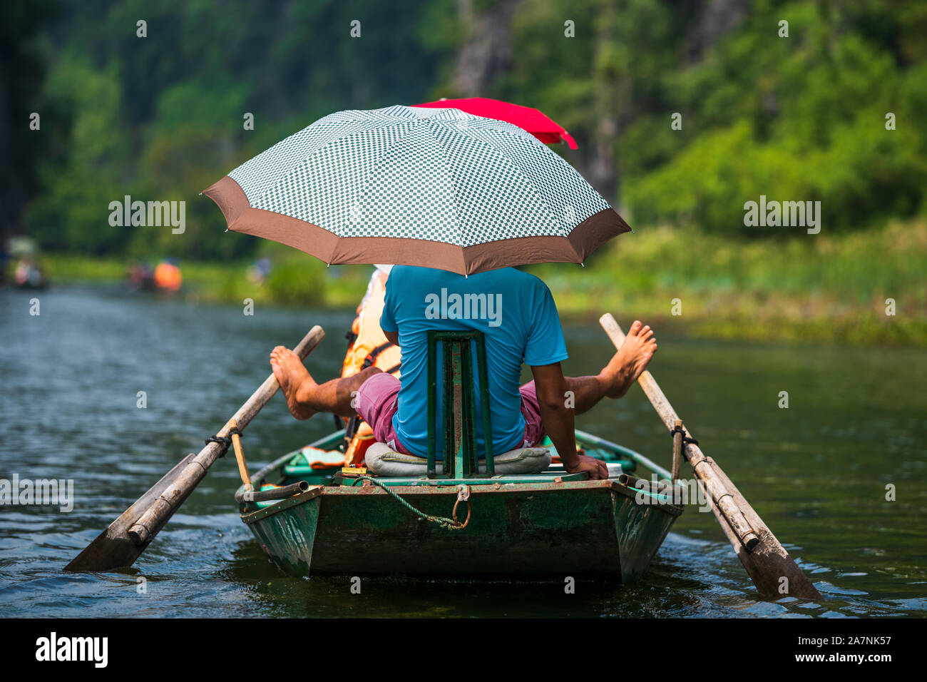 Un vietnamita righe locali una barca a remi con i suoi piedi per i turisti che per i loro viaggi su un giro in barca attraverso le grotte di pietra calcarea di Ninh Binh Foto Stock