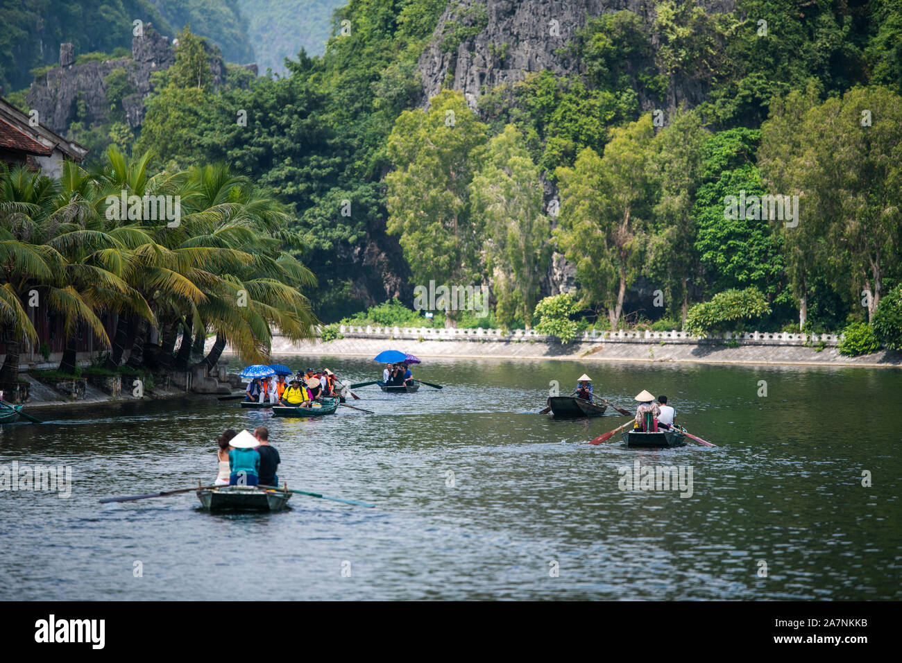 Il vietnamita locali fila imbarcazioni a remi con i loro piedi per i turisti che per i loro viaggi su un giro in barca attraverso le grotte di pietra calcarea di Ninh Binh Foto Stock