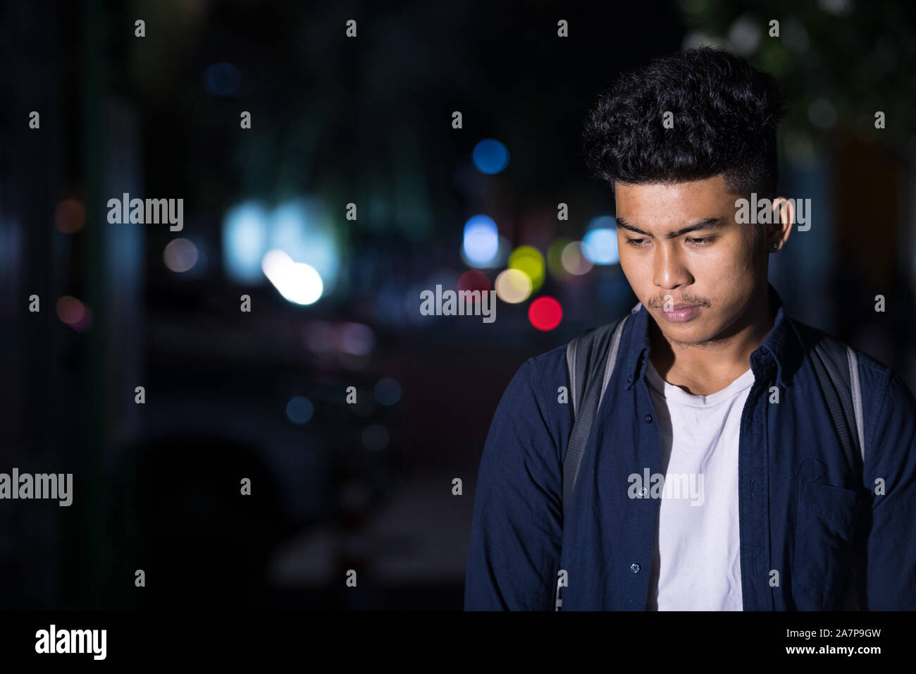 Sottolineato giovane uomo asiatico pensando mentre guardando in giù per le strade della città di notte Foto Stock