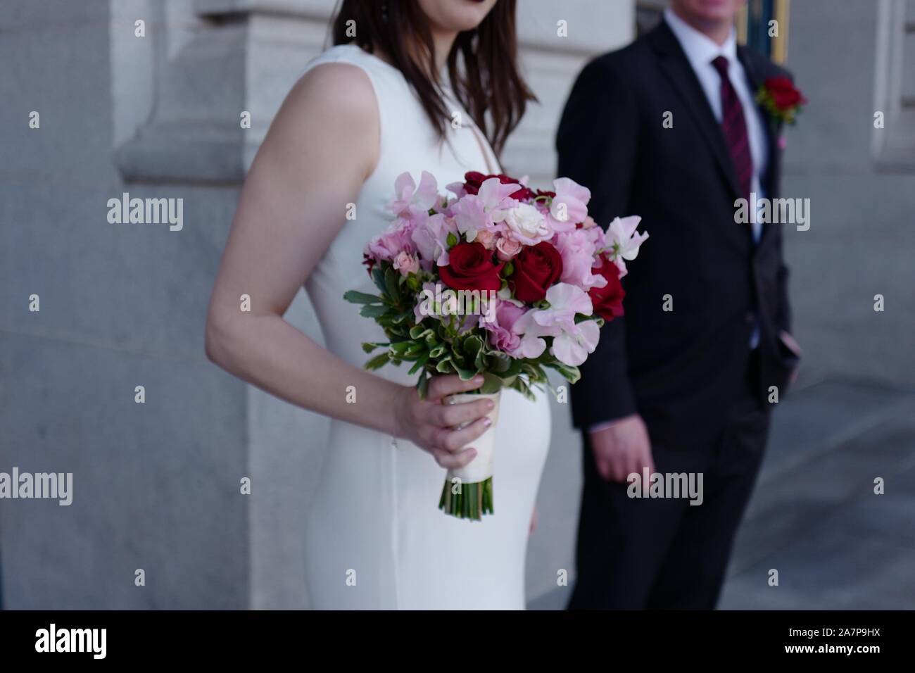 Anonimo ritratto di una sposa in un abito bianco, ovviamente incinta azienda rosa e rosso bouquet di rose in piedi accanto a lo sposo in abito nero Foto Stock