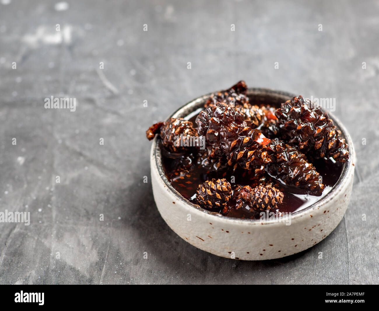 Deliziosa marmellata con baby pigne in una piccola ciotola. Siberiano tradizionale dessert - giovani pigne inceppata sul grigio sfondo a trama. Foto Stock