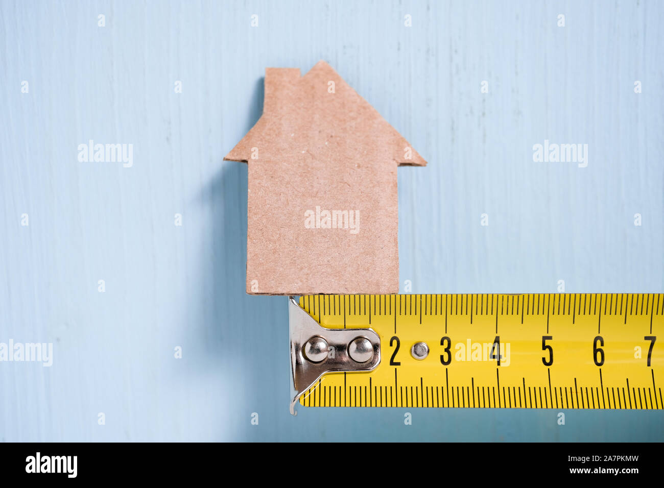 Ritaglio di cartone casa di metallo sul nastro di misurazione di legno su sfondo blu. Concetto di misurazione, budget, riparazione. Foto Stock