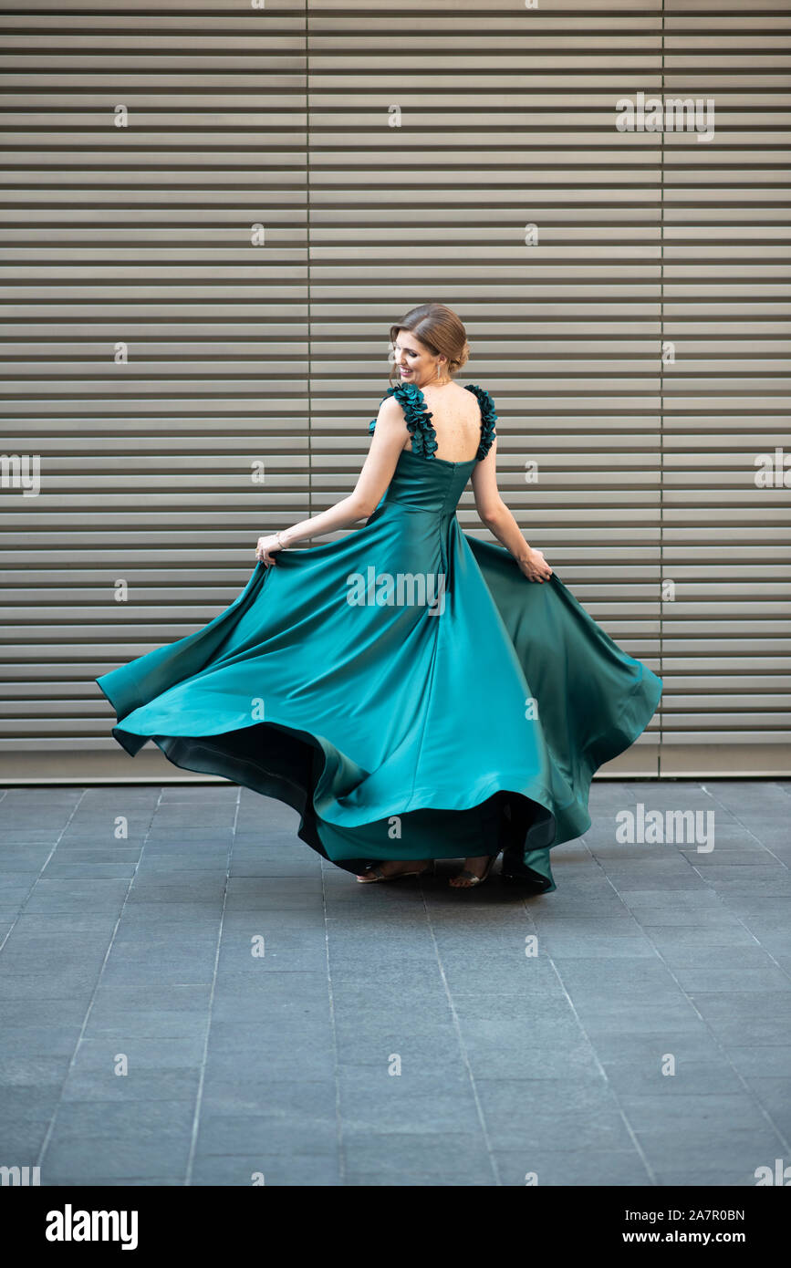 Happy woman dancing in gree abito da sera all'aperto Foto Stock