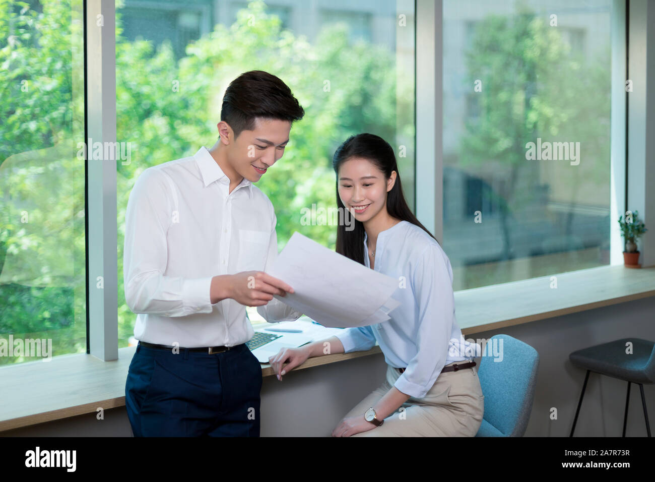 Vita fino colpo di due sorridente maschio e femmina gli imprenditori con i capelli neri la lettura di un documento in un ufficio Foto Stock