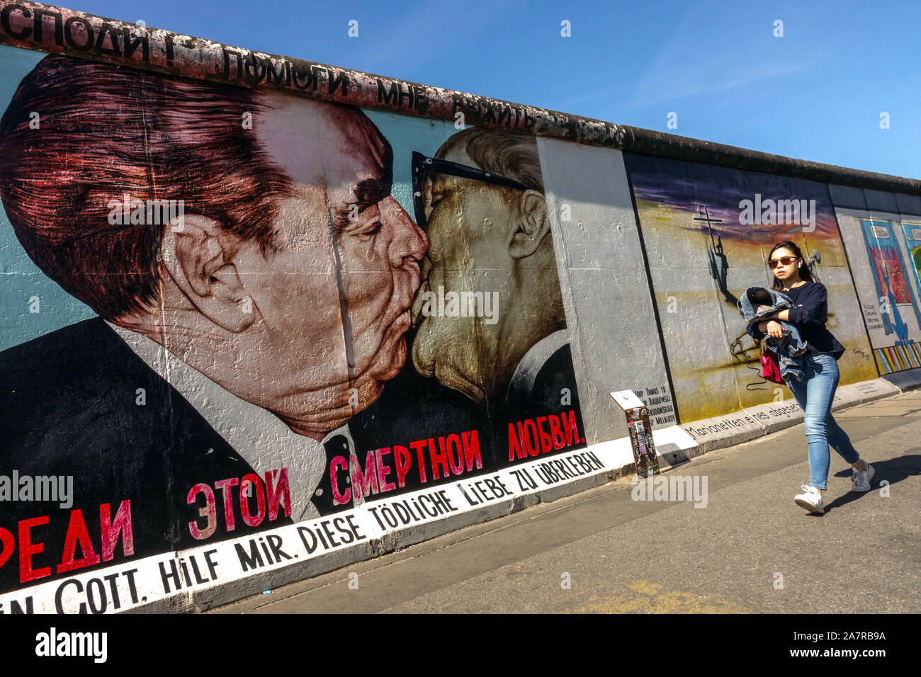 Muro di Berlino, giovane donna asiatica che passa intorno East Side Gallery, Brezhnev Honecker Kiss Germania Friedrichshain città strada Foto Stock