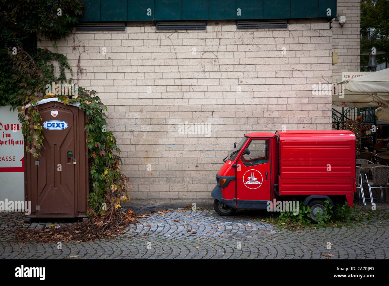 Portable Dixi wc e un Ape Piaggio veicolo commerciale leggero nella parte vecchia della città di Colonia, Germania. Dixi Klo und Piaggio Ape Kleintranspor Foto Stock