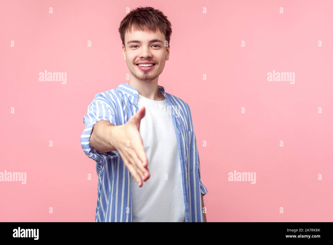 Ritratto di Allegro friendly i capelli castani uomo con piccola barba e baffi in casual Camicia a Righe dando la mano per stretta di mano e sorridente in telecamera. i Foto Stock