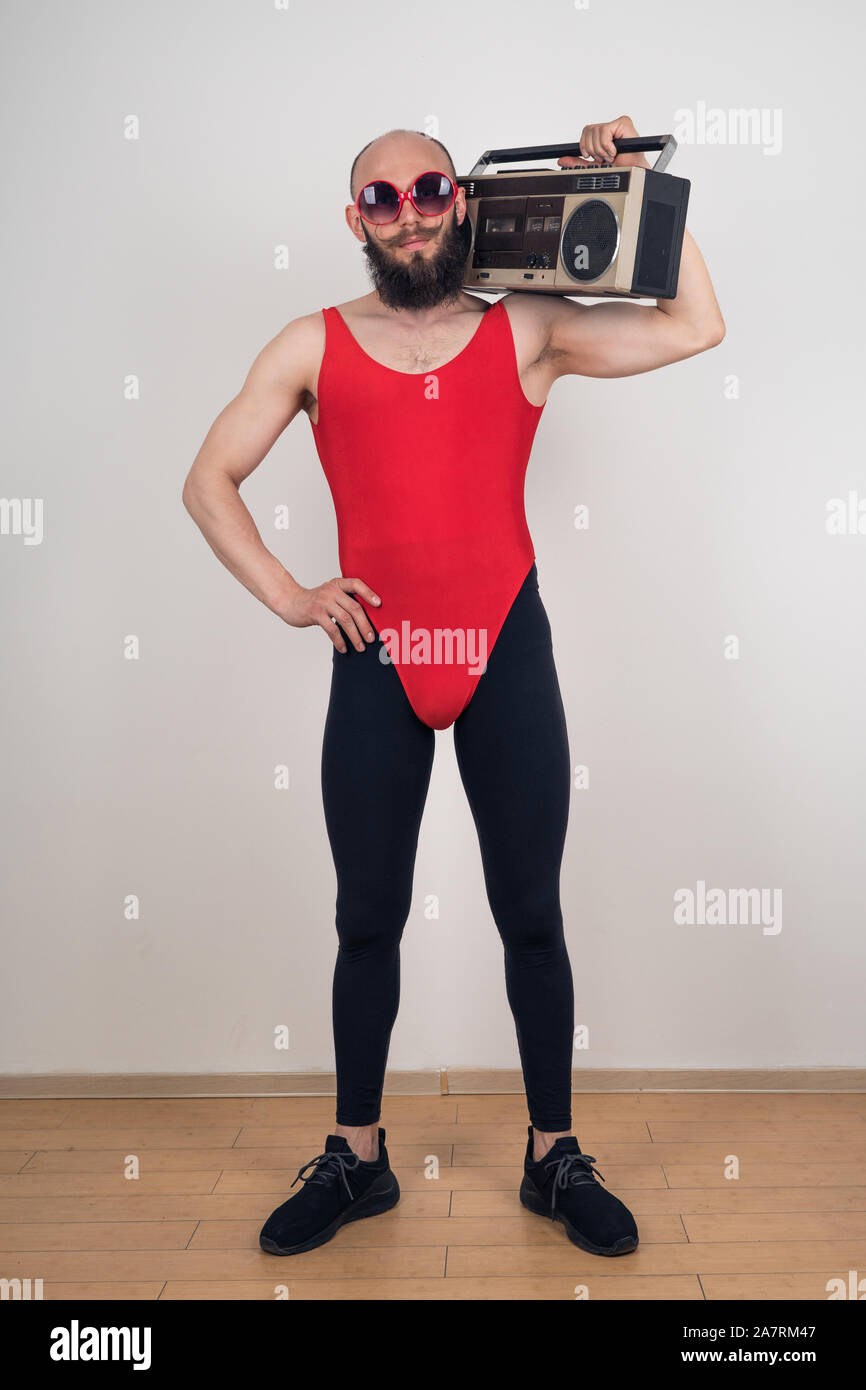 Un uomo vestito per la discoteca-retrò parti. Funny barbuto ragazzo in occhiali da sole e leggings con red body con retro registratore a nastro Foto Stock