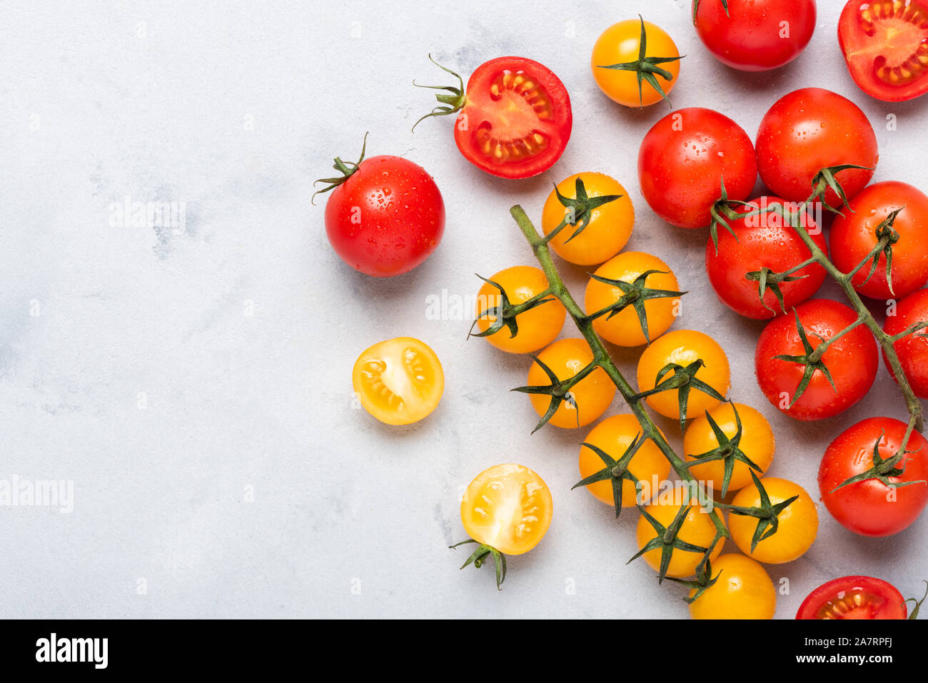 Piccoli pomodori ciliegia assortimento, freschi maturi rossi sul ramo, rosso e giallo, intere e tagliate a metà, sul tavolo rustico laici piatta con copia spazio. Foto Stock