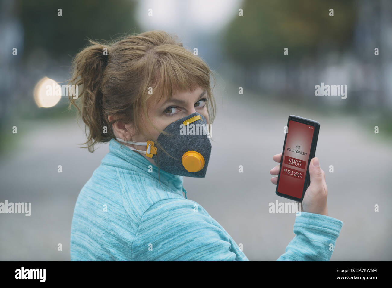 Donna che indossa un vero e proprio anti-inquinamento, anti-smog virus e la maschera per il viso e il controllo della corrente inquinamento atmosferico con smart phone app Foto Stock