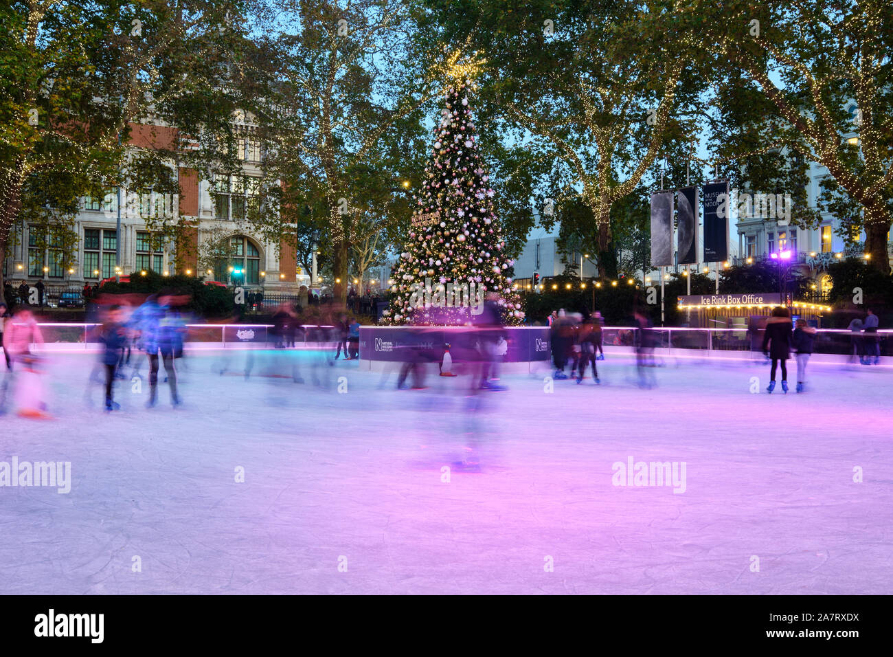 Sfocatura Movimento immagine di persone pattinaggio sul Natale decorato pista di pattinaggio su ghiaccio a Londra il Museo di Storia Naturale al crepuscolo, intorno al centro di albero di natale. Foto Stock