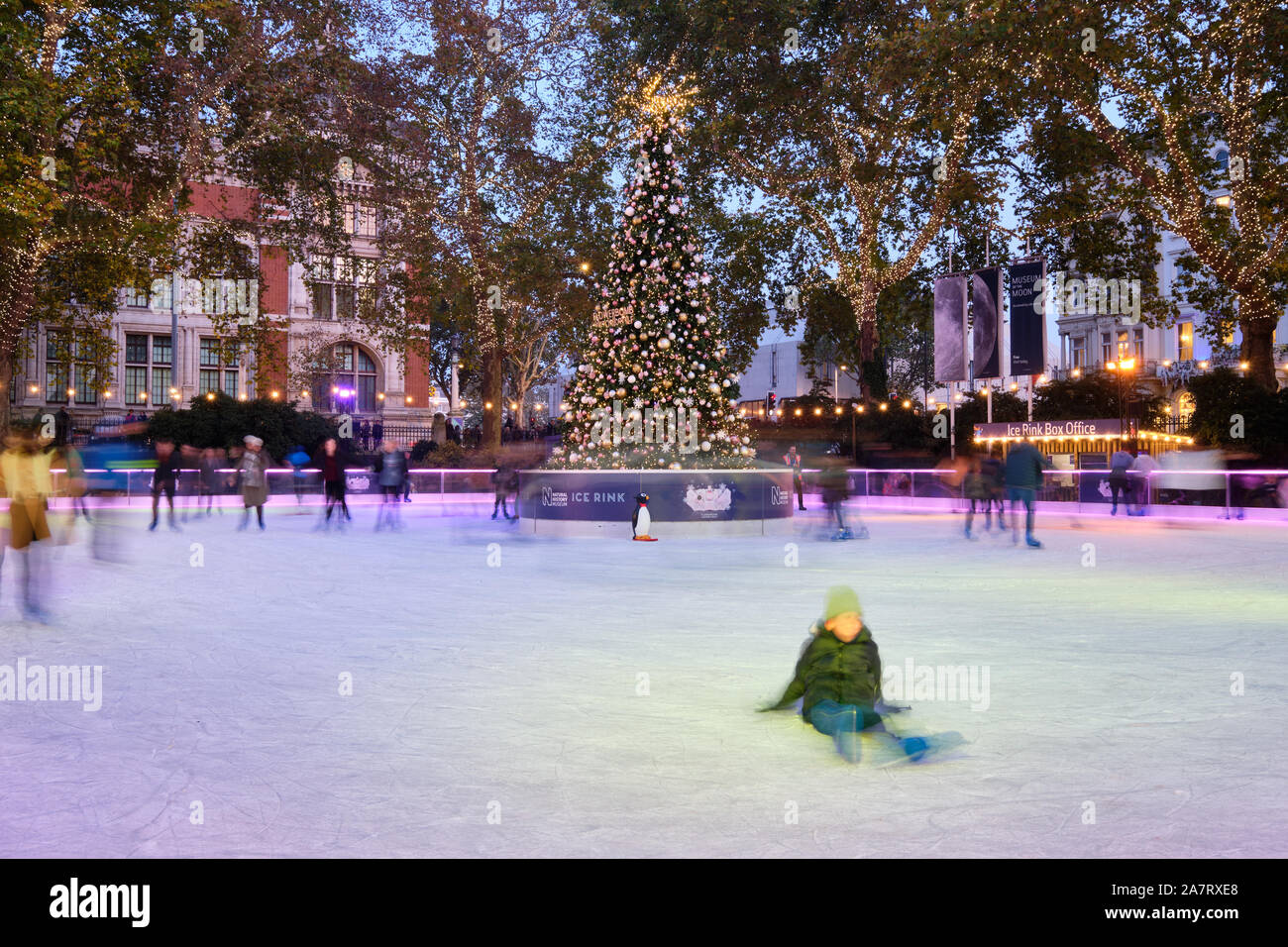 Sfocatura Movimento immagine di persone pattinaggio sul Natale decorato pista di pattinaggio su ghiaccio a Londra il Museo di Storia Naturale al crepuscolo, intorno al centro di albero di natale. Foto Stock