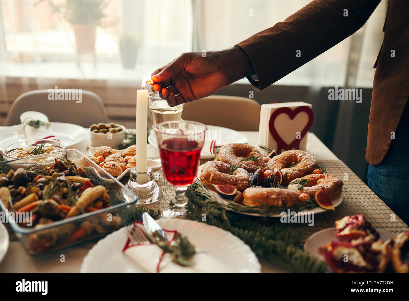 Primo piano della mano candela di illuminazione più rustico tavola di Natale con delizioso cibo fatto in casa decorata con rami di abete, spazio di copia Foto Stock