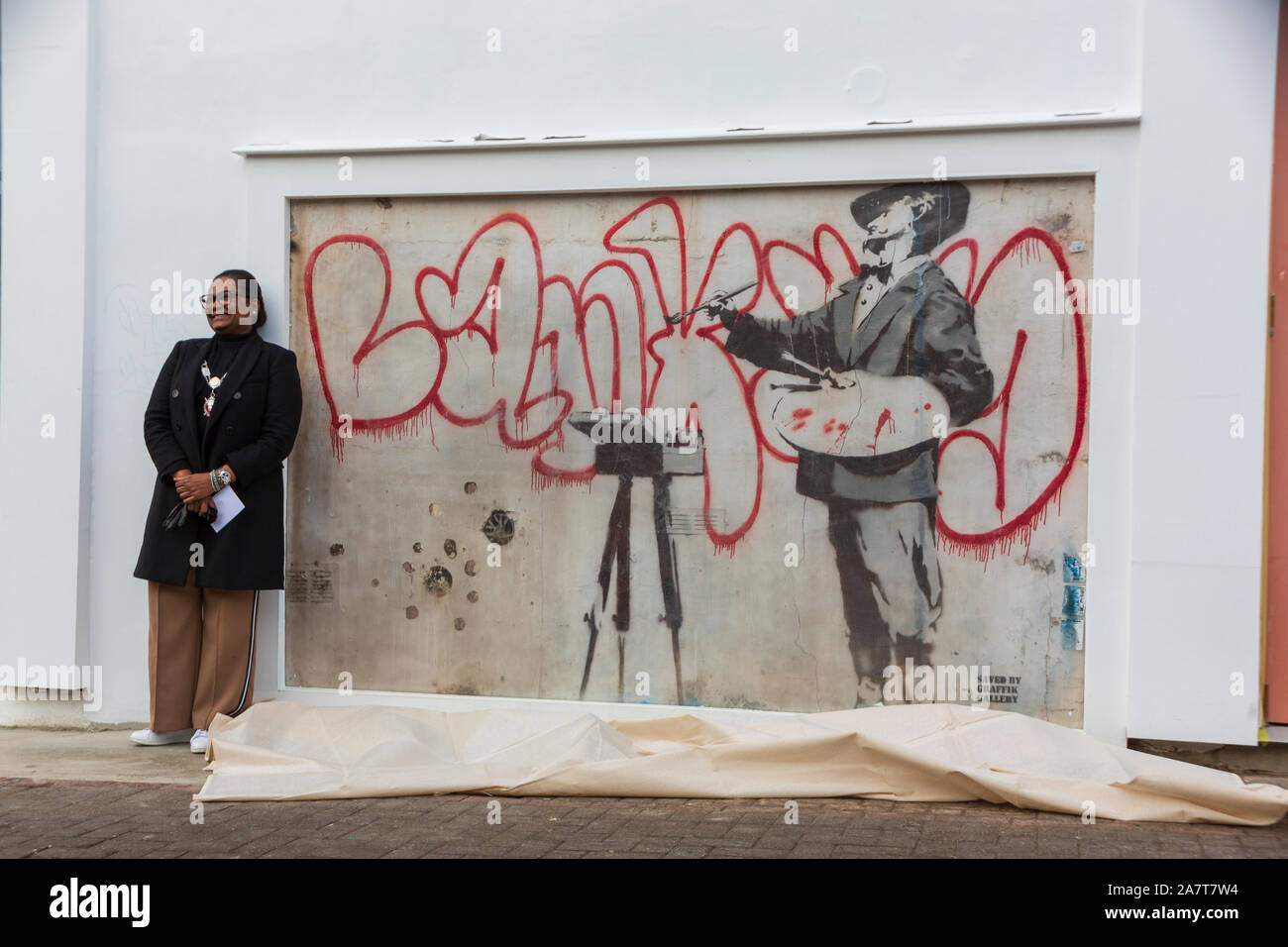 Londra, Regno Unito. 4 Ott 2019. Restaurato recentemente Banksy illustrazione 'Graffiti pittore' rivelato da Royal Borough di Kensington e Chelsea Vice Sindaco Cllr Walaa Idris, e capitale Enstar CEO Simon Lione a Londra Notting Hill. Il Banksy artwork restaurato da Enstar rimarrà sul display permanente per la comunità. Situato all'angolo della strada Ackam e Portobello Road, stencil artwork "Graffiti pittore' rappresenta il Barocco spagnolo pittore Diego Velasquez dipinto "BANKSY" in vernice rossa su un timpano bianco parete. Credito: thamesfleet/Alamy Live News Foto Stock