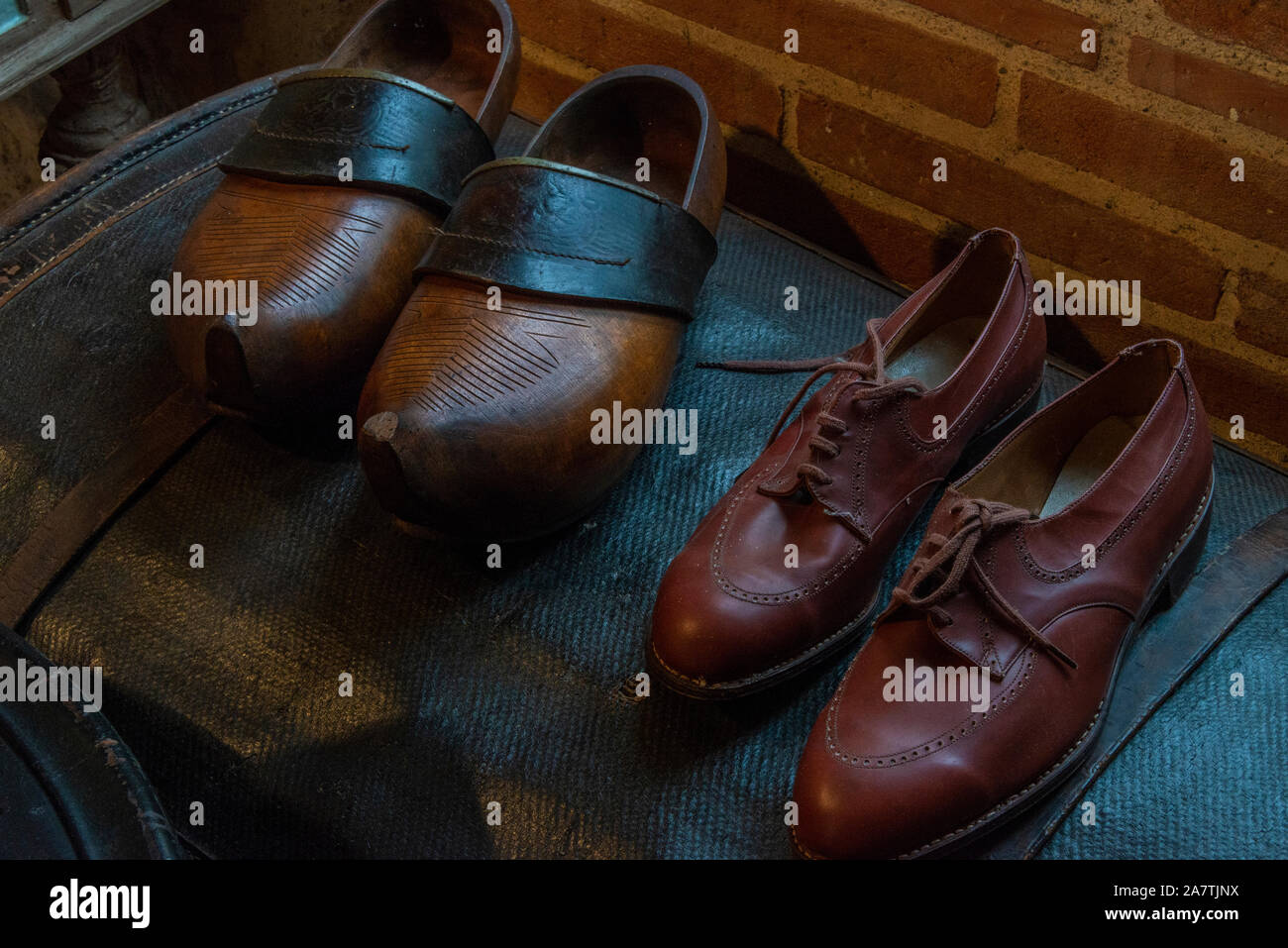 Una chiusura su un paio di zoccoli di legno, e scarpe in pelle, illuminato da luce naturale della finestra. Foto Stock