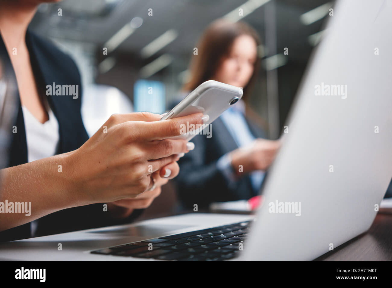 Close-up di mani femminili tenere lo smartphone moderno presso il suo posto di lavoro presso l'ufficio. Un gruppo di uomini di affari che lavorando insieme e utilizzando i gadget digitali a ope Foto Stock