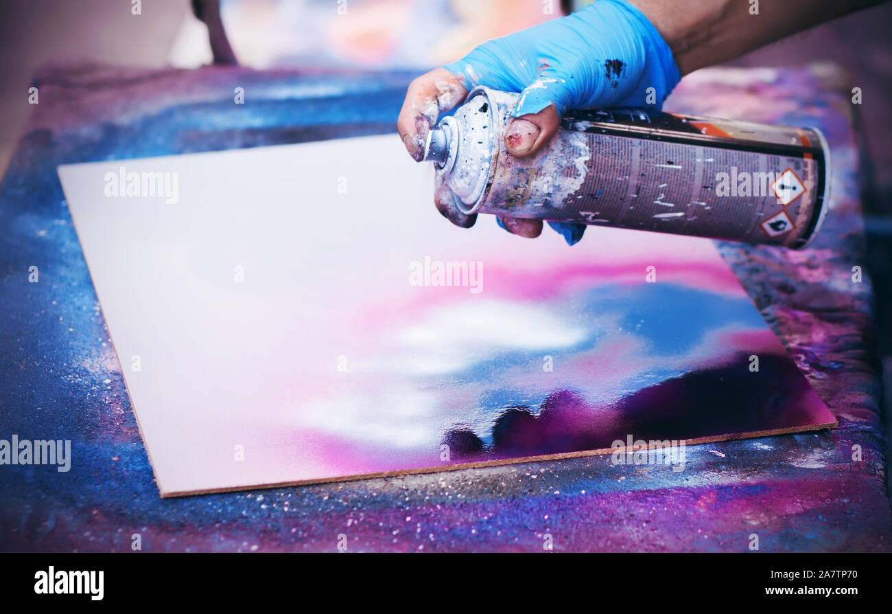 Un artista di strada in guanti strappato spray-vernici graffiti su una tela bianca in colori luminosi. Foto Stock