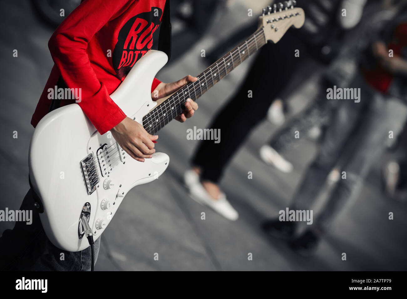 Un giovane musicista di strada in una t-shirt rossa riproduce la musica rock su un bianco di chitarra elettrica, in piedi nel mezzo di una strada affollata. Foto Stock