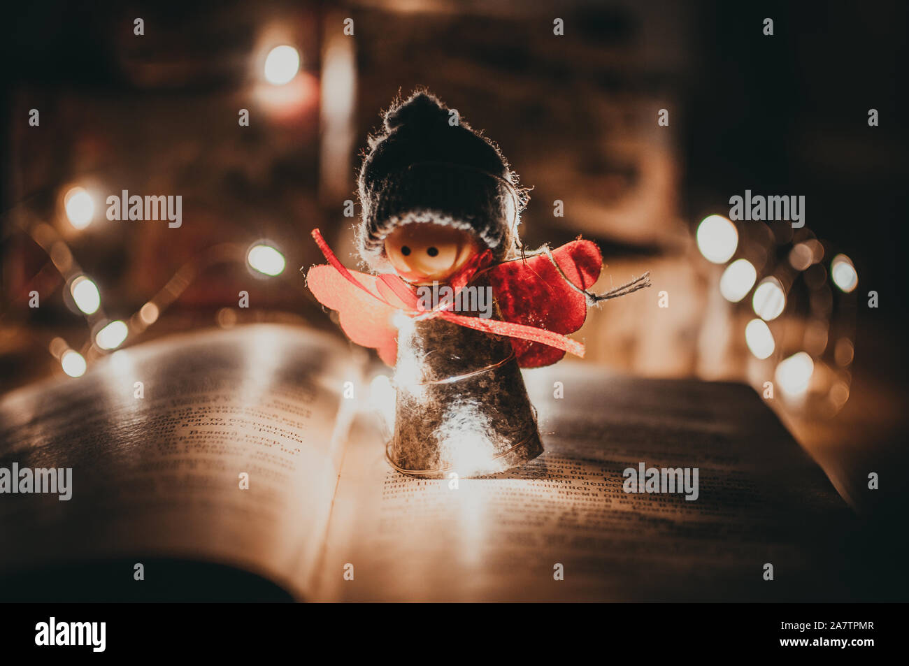 Angelo in legno ghirlanda di Natale si erge su un libro, in background è un LED ghirlanda. Vacanze di Natale del concetto. Foto Stock