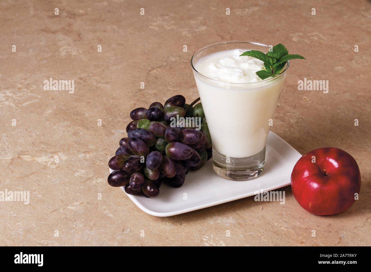 Il Kefir in un calice di vetro con un ramo di menta con Apple e di mosti di uve su una tavola di legno su uno sfondo marrone Foto Stock