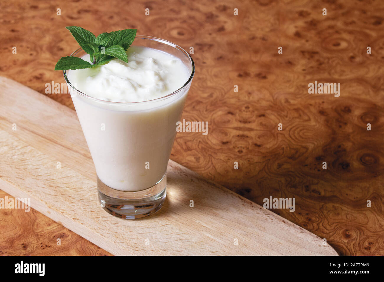 Il Kefir in un calice di vetro con un ramo di menta su una tavola di legno su uno sfondo marrone Foto Stock