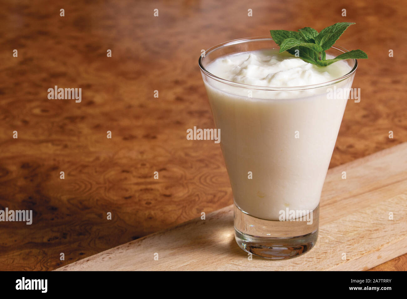 Il Kefir in un calice di vetro con un ramo di menta su una tavola di legno su uno sfondo marrone Foto Stock