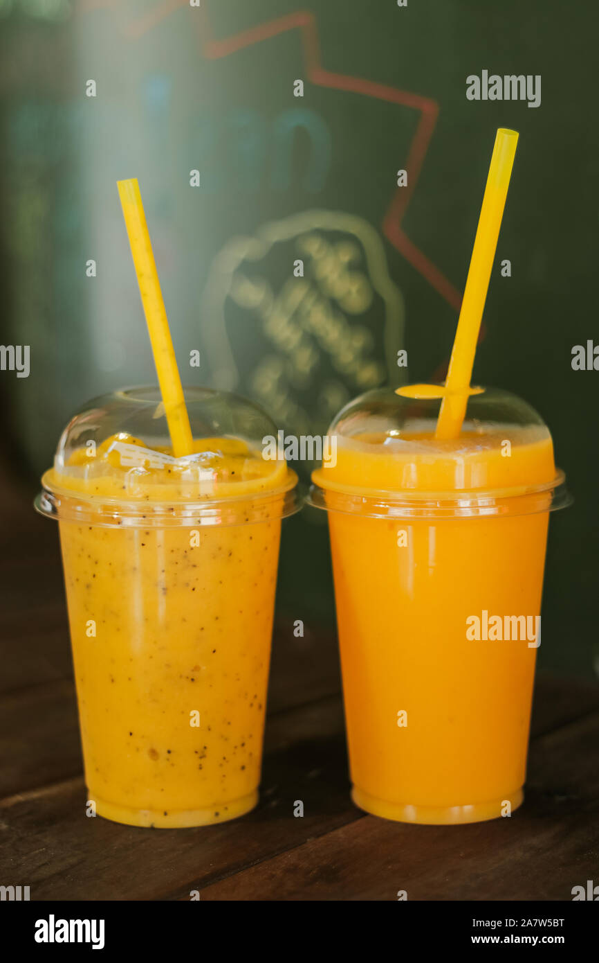 Mango e frullato maracuya in i bicchieri di plastica usa e getta con cannucce su una tavola di legno in una caffetteria. Copyspace. Foto Stock