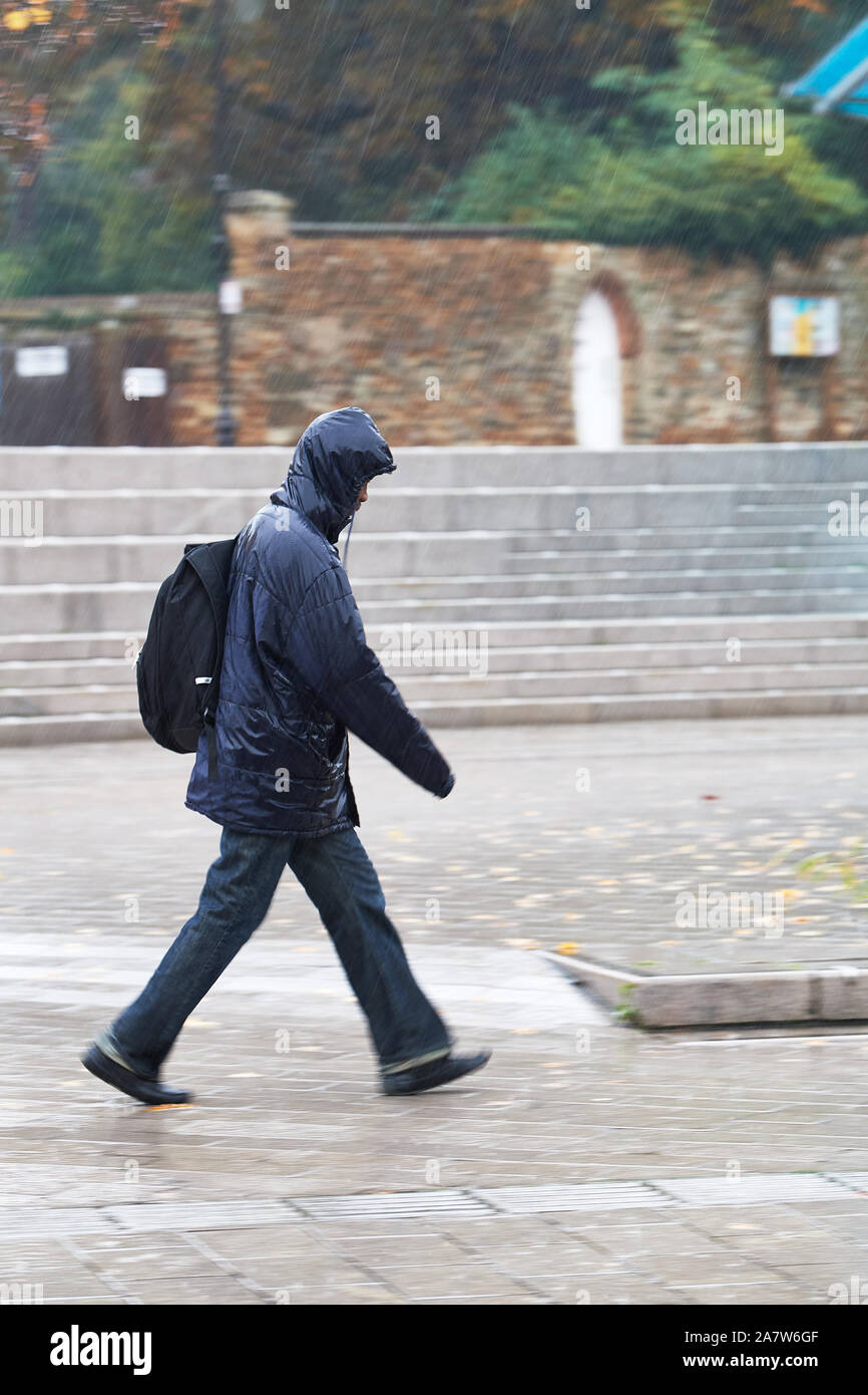 Intriso di un uomo cammina lungo il marciapiede accanto alla piazza del mercato (luogo) durante un acquazzone sul bagnato, giorno piovoso al centro della cittadina di Kettering, Northa Foto Stock