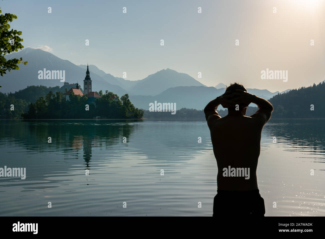 Silhouette di un uomo europeo facendo si allunga la mattina dopo la pratica del metodo di meditazione e di respirazione profonda Wim Hof , mentre il bagno nel lago di Bled. Foto Stock
