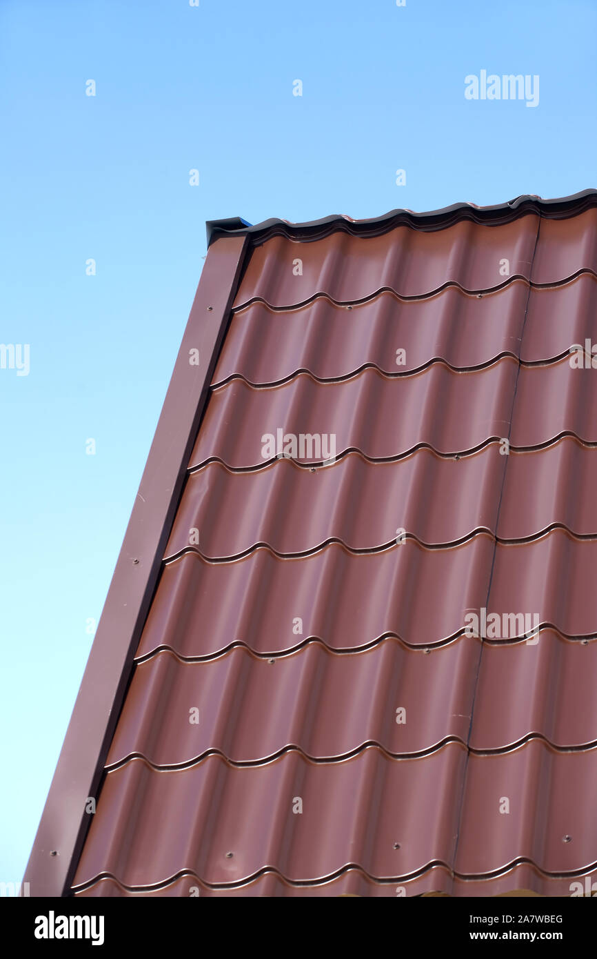 Frammento di country house il tetto dalla brown Piastrella in metallo sotto il chiaro cielo blu senza nuvole. Vista verticale closeup Foto Stock