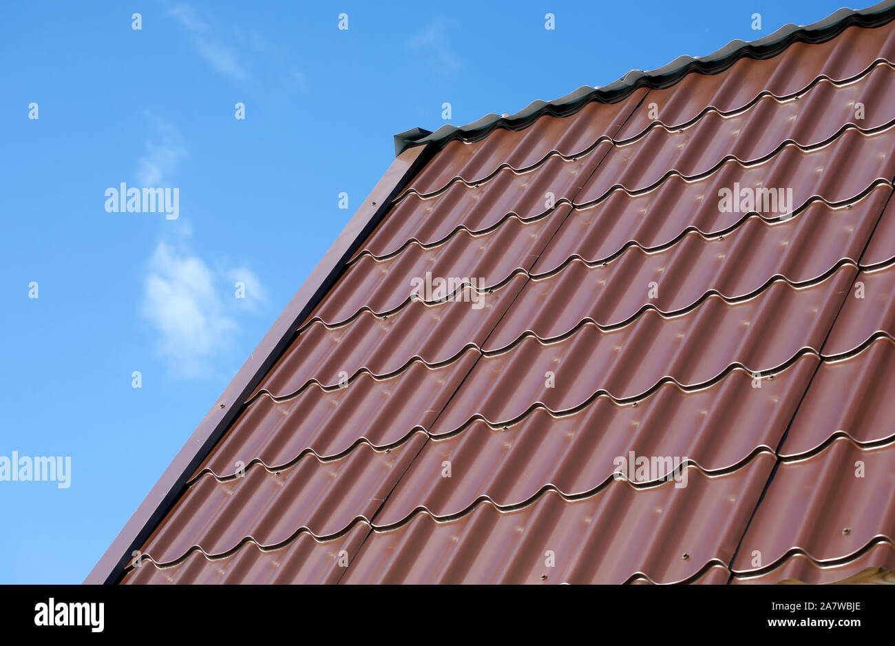 Parte della casa di campagna del nuovo tetto marrone dalla piastrella in metallo sotto il cielo blu con nuvole bianche. Vista orizzontale closeup Foto Stock