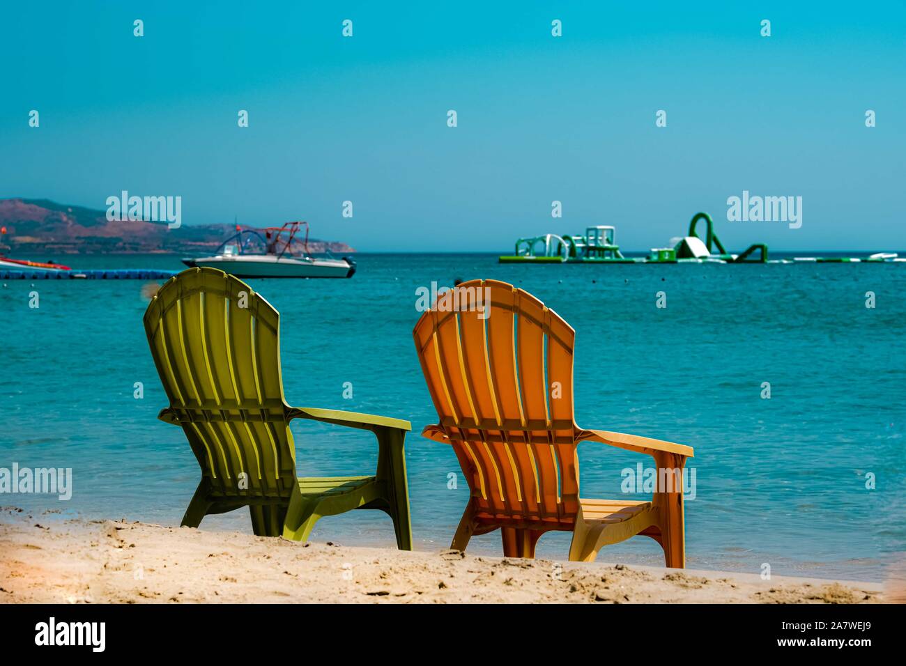 Due sedie colorate in spiaggia, di fronte al mare blu. Foto Stock