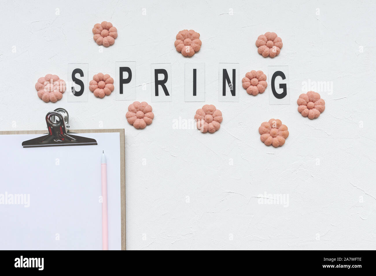 Parola di primavera e fiore di cookie, carta e penna su uno sfondo bianco. Vacanze di primavera per la cottura e di fare il concetto di elenco. Vista superiore, piana, laici mockup, socia Foto Stock