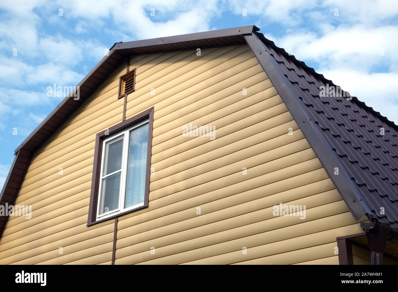 La sezione superiore della moderna casa di campagna privata parete ricoperta con schierandosi giallo e marrone e tetto metallico sul cielo blu con nuvole sulla giornata soleggiata vista frontale vicino Foto Stock