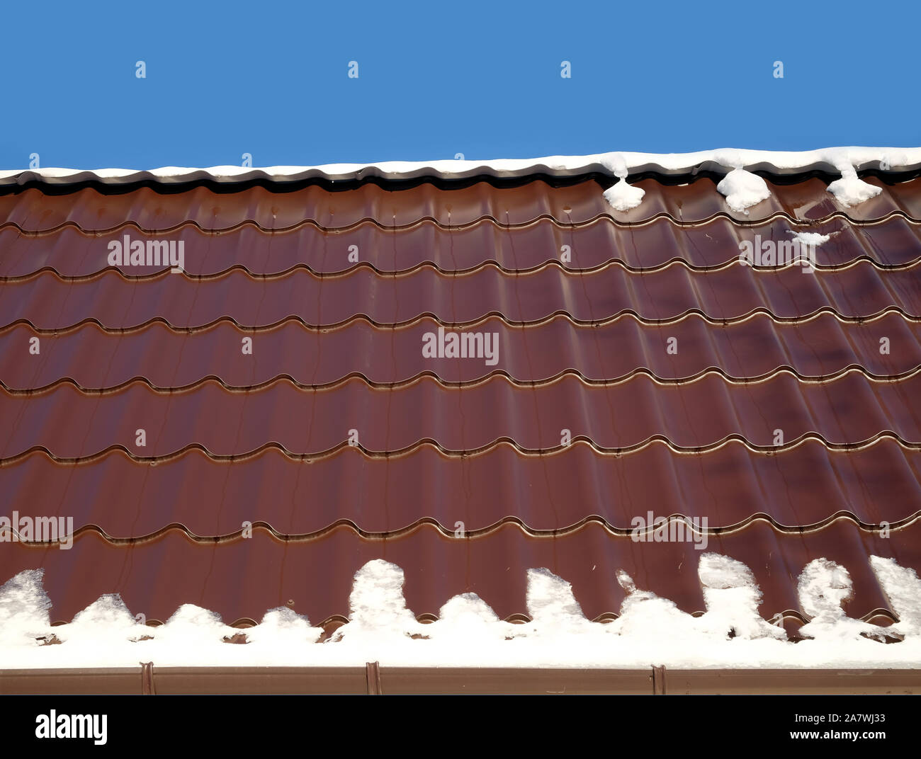 New country house il tetto dalla brown Piastrella in metallo con fusione della neve in primavera sotto il chiaro cielo blu senza nuvole. Vista orizzontale closeup Foto Stock