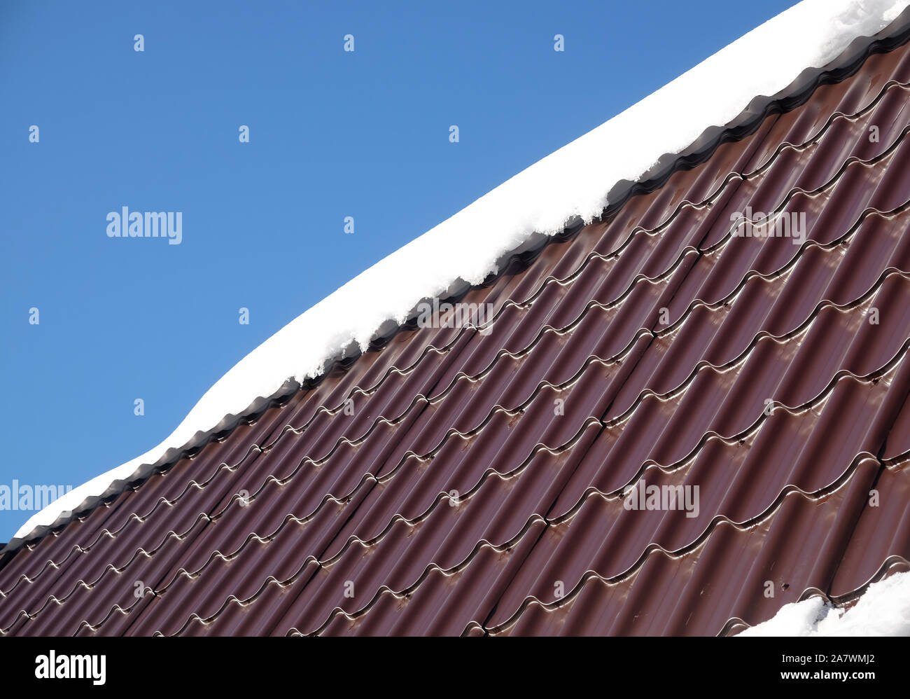 Lato del country house il tetto dalla brown Piastrella in metallo con cumulo di neve nella soleggiata giornata di primavera sotto il blu cielo senza nuvole vista laterale Foto Stock