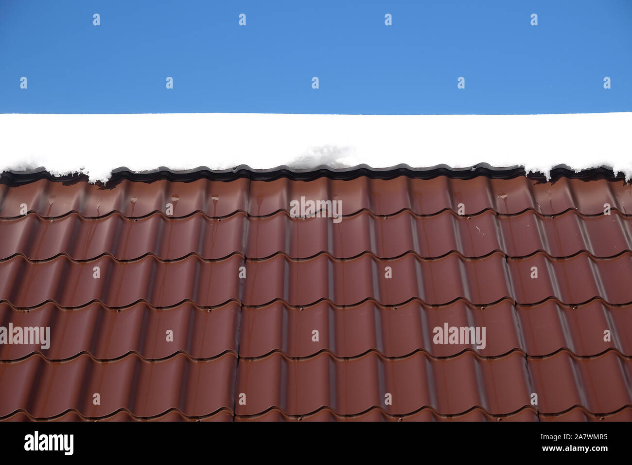 Lato del country house il tetto dalla brown Piastrella in metallo con neve nella soleggiata giornata di primavera sotto il cielo blu con nuvole bianche vista frontale Foto Stock