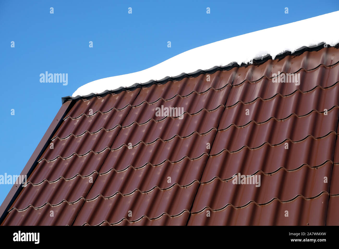 Lato del country house il tetto dalla brown Piastrella in metallo con cumulo di neve nella soleggiata giornata di primavera sotto il cielo blu con nuvole bianche vista laterale Foto Stock
