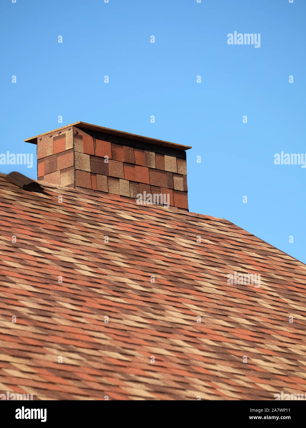 Parte del tetto marrone di una casa coperta con motley soft le assicelle con breve grande fumaiolo di chiudere fino sotto il cielo blu senza nuvole sulla giornata di sole Foto Stock