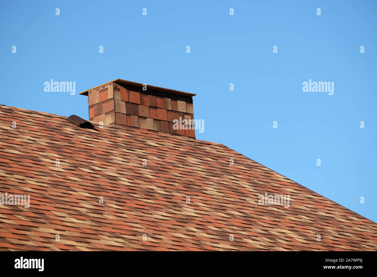 Parte del tetto marrone di una casa coperta con motley soft le assicelle con breve grande fumaiolo di chiudere fino sotto il cielo blu senza nuvole sulla giornata di sole Foto Stock