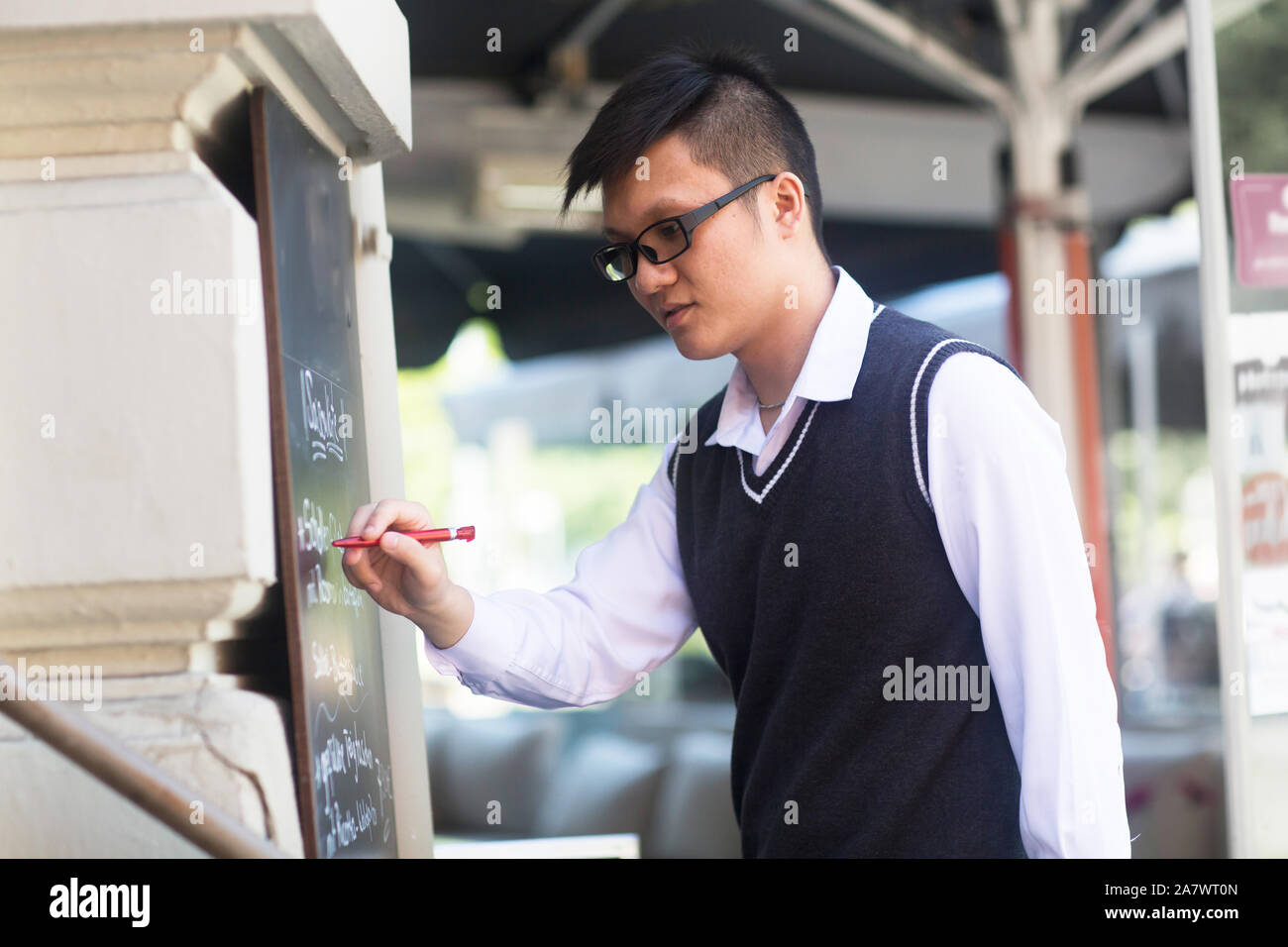 Young Asia cameriere in un bar di scrivere nuove offerte Foto Stock