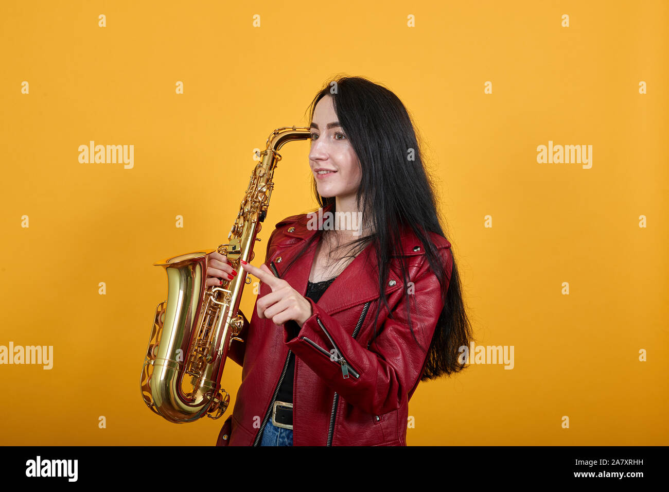 Giovane e bella donna che guarda, puntare il dito indice in disparte, mantenendo il sassofono Foto Stock