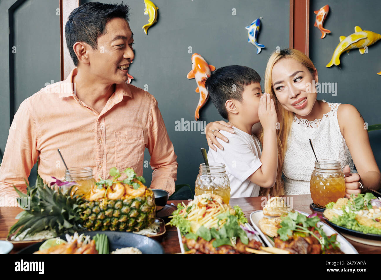 Adorabili poco Asian boy whispering segreto di sua madre durante la cena di famiglia in cafe Foto Stock