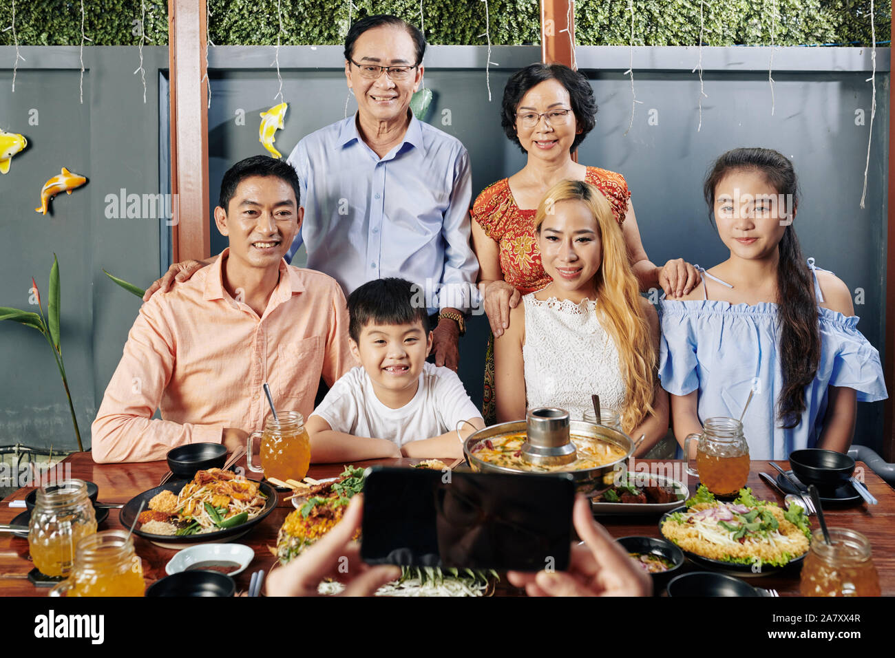 Felice grande famiglia vietnamita che pongono al grande tavolo da pranzo per foto sullo smartphone Foto Stock