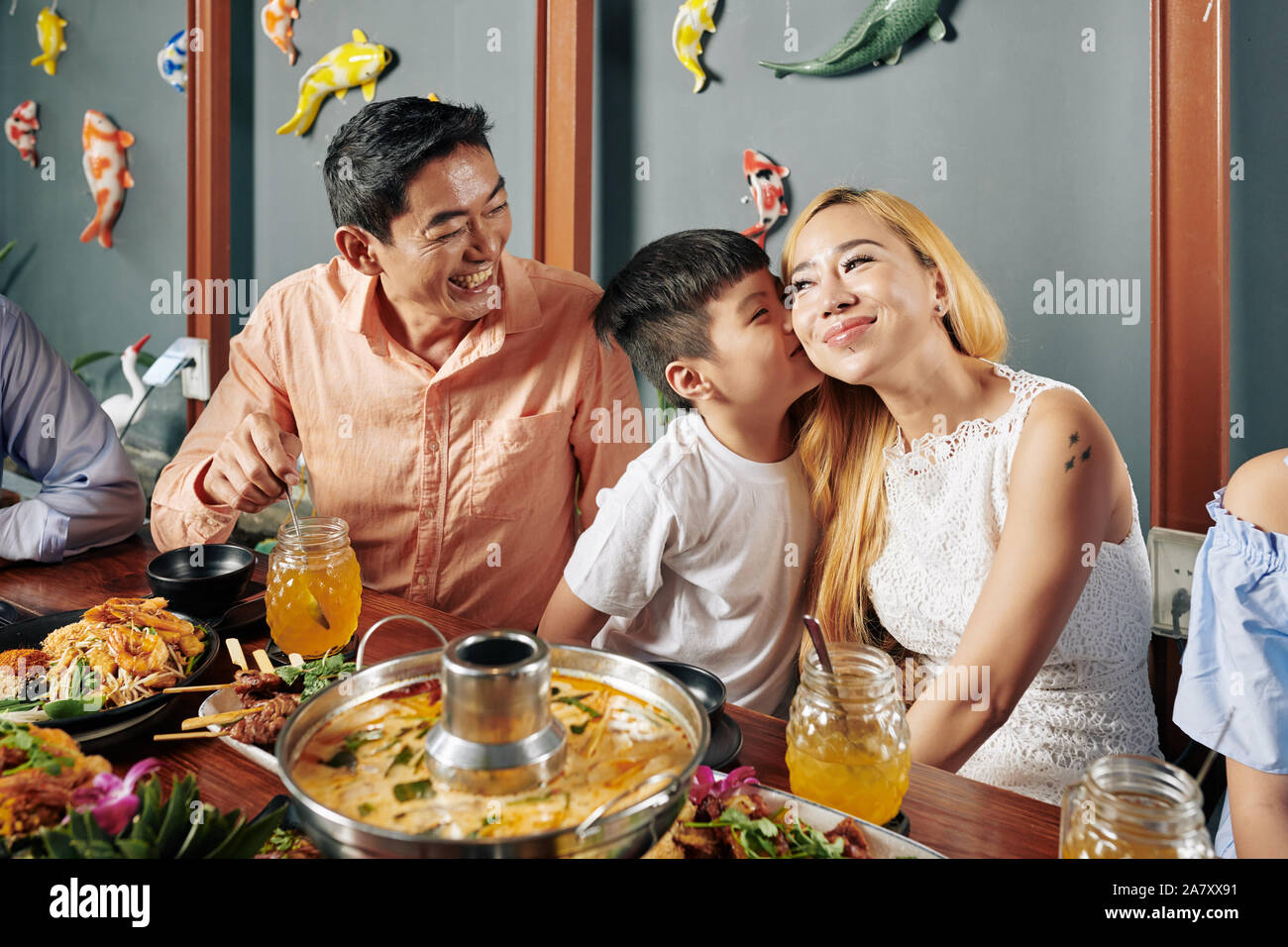 Felice piccolo grazioso ragazzo vietnamita di baciare la sua bella sorridente madre sulla guancia quando essi sono familiari aventi la cena in ristorante Foto Stock