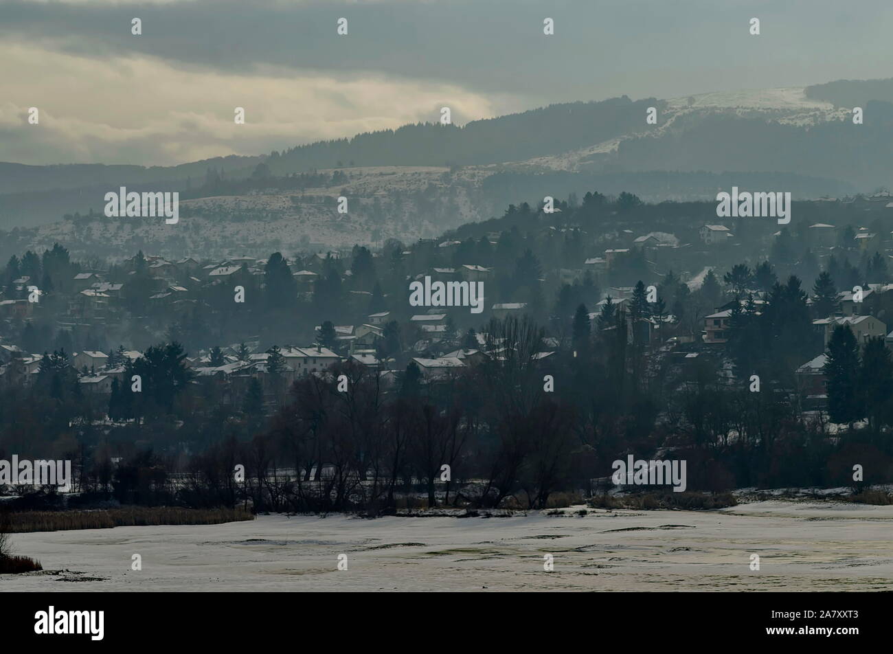Scena invernale con lago ghiacciato, montagna innevata, glade, foresta e residenziale quartiere di borgo bulgaro Pancharevo, Sofia, Bulgaria Foto Stock