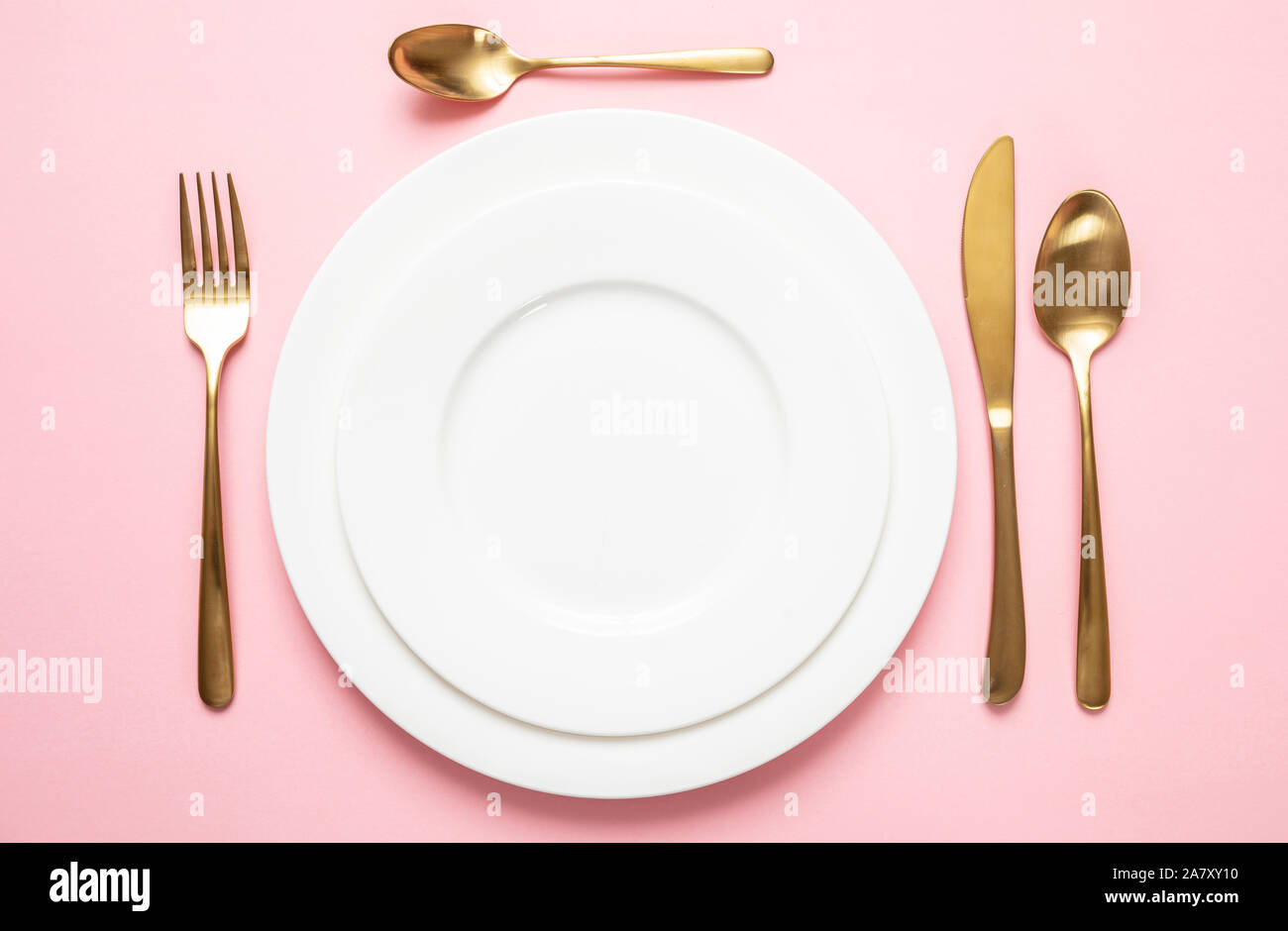 Oro e rosa lussuoso impostazione tabella. Golden set di posate e piatti bianchi contro sfondo rosa. Vista superiore, spazio di copia Foto Stock