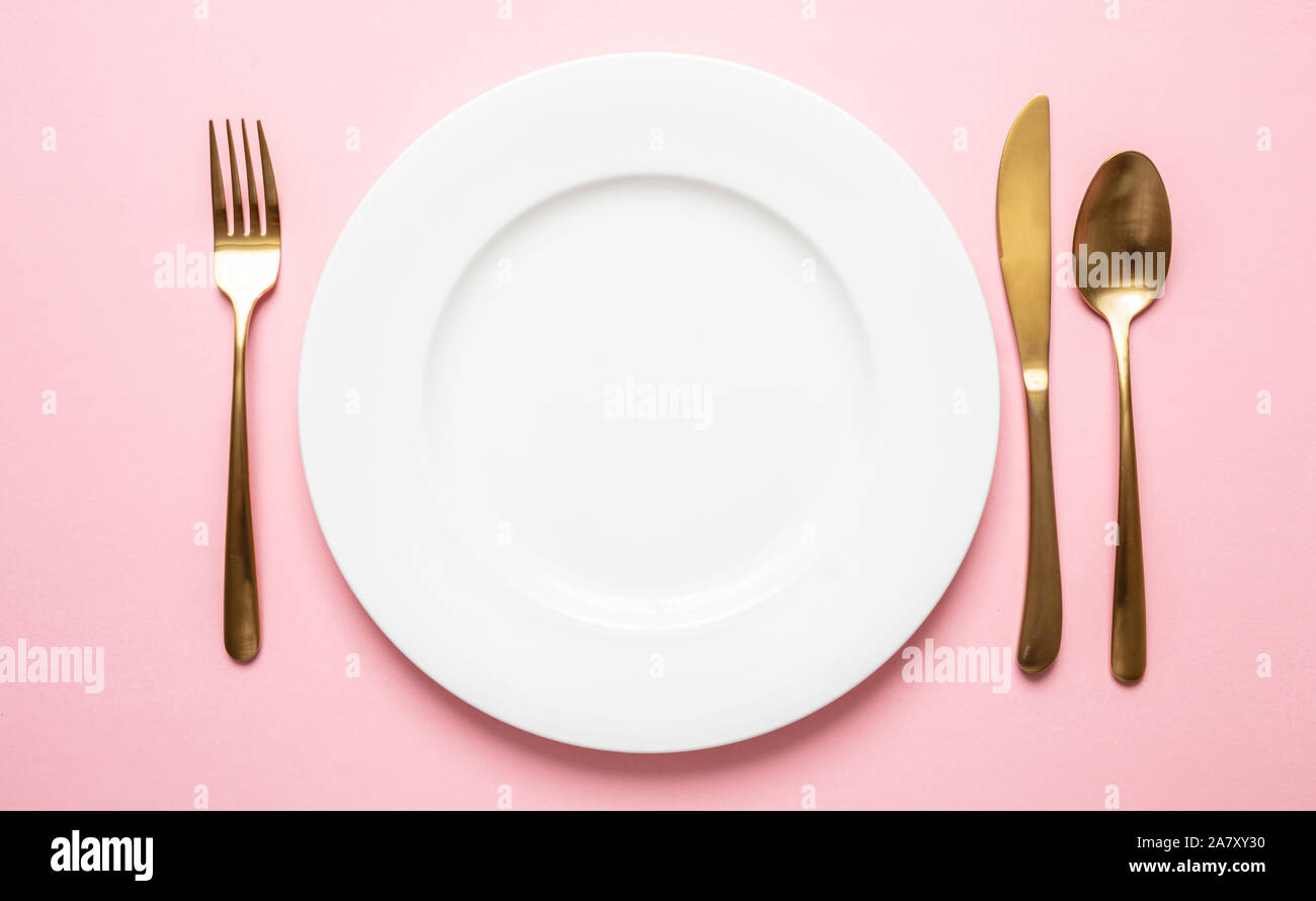 Oro e rosa lussuoso impostazione tabella. Golden set di posate e piatti bianchi contro sfondo rosa. Vista superiore, spazio di copia Foto Stock